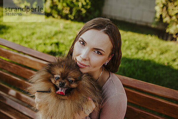 Lächelnde Frau sitzt mit Hund auf Bank