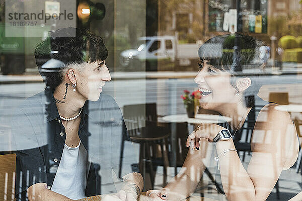 Happy young couple talking in cafe seen through glass