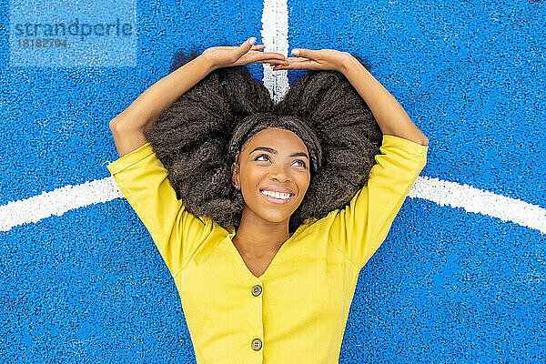 Glückliche junge Frau mit Afro-Frisur liegt auf blauem Basketballplatz