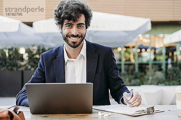 Hübscher Geschäftsmann mit Dokument und Laptop  der im Café arbeitet
