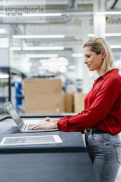 Lächelnde Geschäftsfrau mit Laptop in der Fabrik