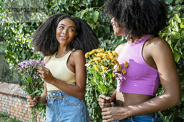 Glückliche Freundinnen halten Blumen vor der Pflanze