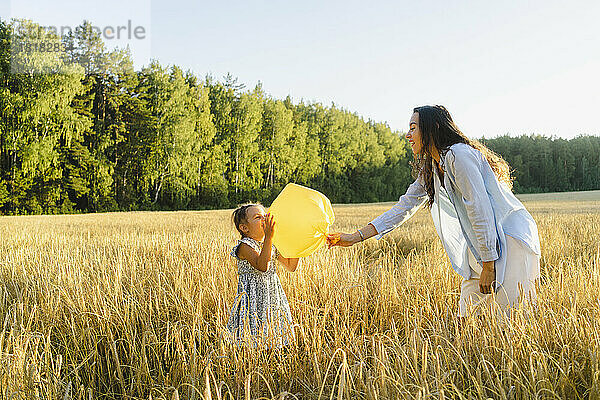 Verspielte Frau mit Tochter  die einen Müllsackballon hält und auf dem Feld steht