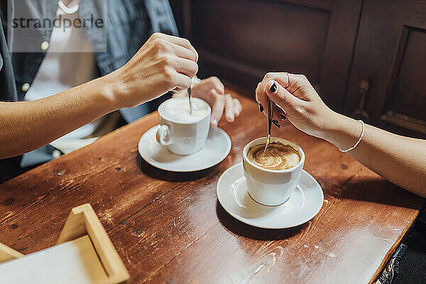 Hände eines jungen Paares  das im Café Kaffee rührt