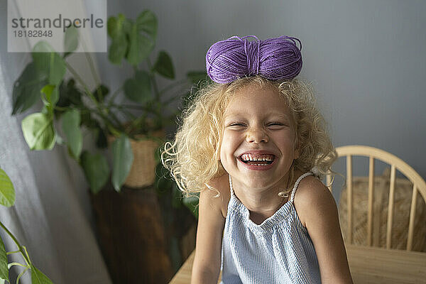 Happy girl balancing ball of wool on head at home