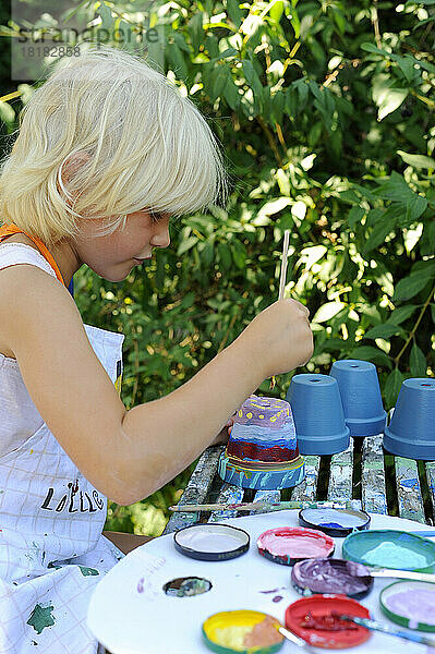 Little girl painting flower pots in garden