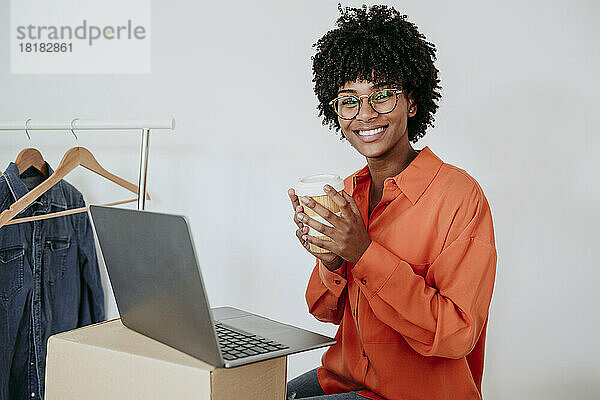 Glückliche Geschäftsfrau mit Laptop und Kaffeetasse sitzt im Heimbüro