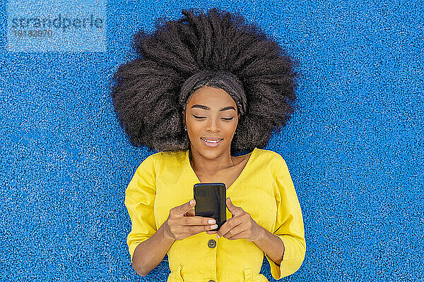 Frau mit Afro-Frisur benutzt Smartphone und liegt auf blauem Basketballplatz