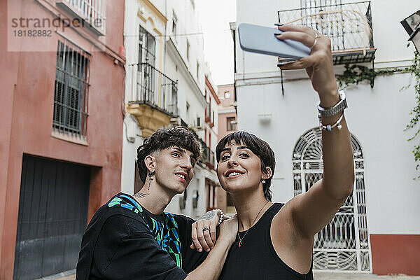 Lächelnde Frau mit Freund macht Selfie mit dem Handy vor Gebäuden