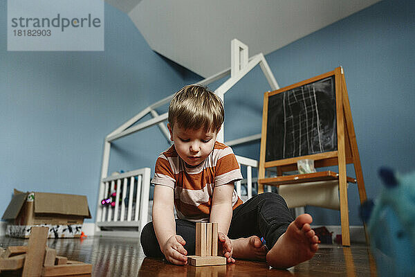 Verspielter Junge spielt mit Holzklotz im Schlafzimmer zu Hause