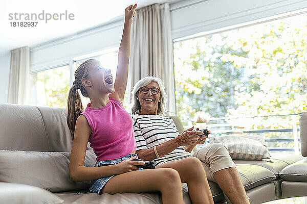 Granddaughter with arm raised screaming by grandmother playing video game at home