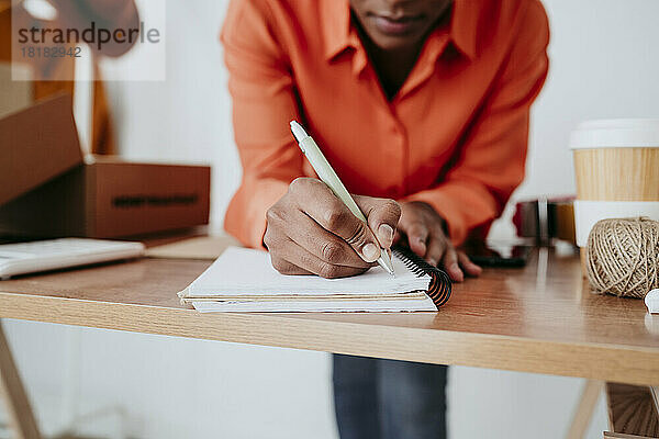 Junge Geschäftsfrau schreibt mit Stift am Schreibtisch Tagebuch