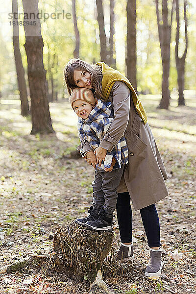 Glücklicher Junge steht mit Mutter auf Baumstumpf im Park