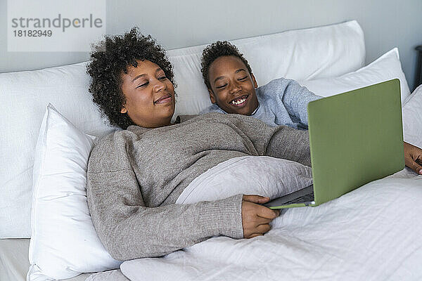 Glücklicher Sohn und Mutter schauen sich im Schlafzimmer einen Film mit Laptop an
