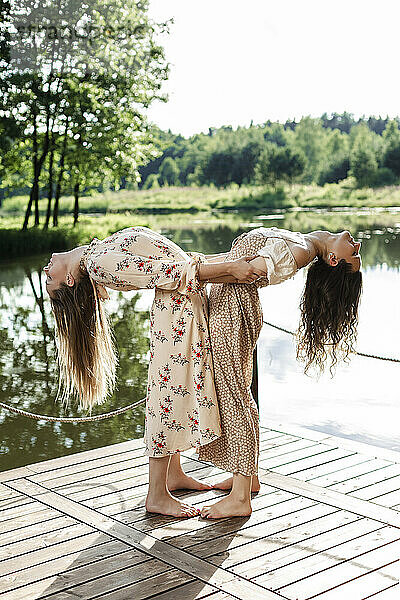 Young friends bending over backwards by holding each other on pier
