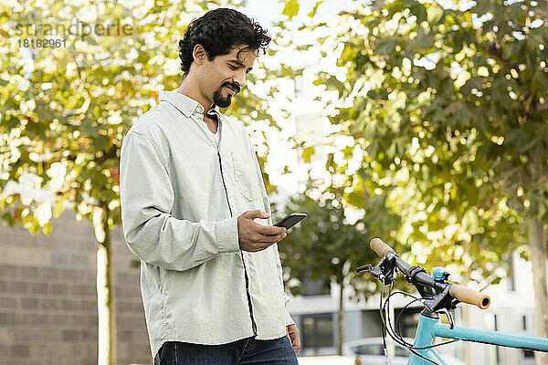 Lächelnder Mann benutzt Smartphone und steht neben Fahrrad