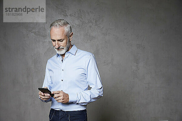 Reifer Mann mit Smartphone vor grauem Hintergrund