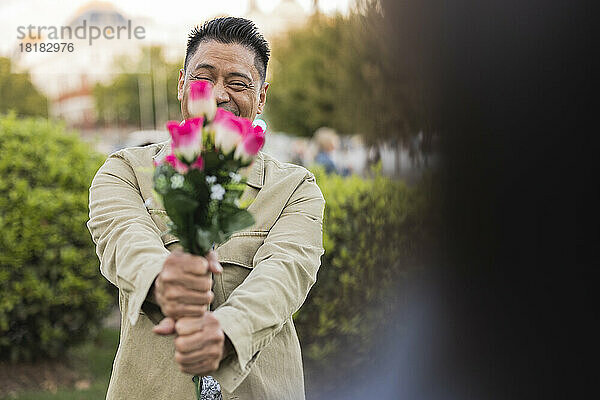 Lächelnder reifer Mann zeigt am Valentinstag Blumen im Park
