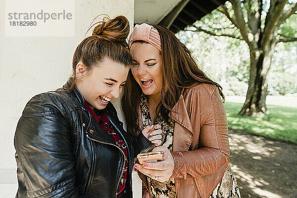 Zwei lachende Freunde schauen auf ihr Handy