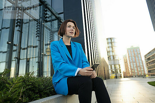 Geschäftsfrau mit Smartphone sitzt vor Bürogebäude