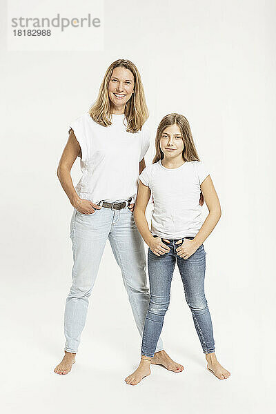 Mother and daughter with hands in pockets against white background