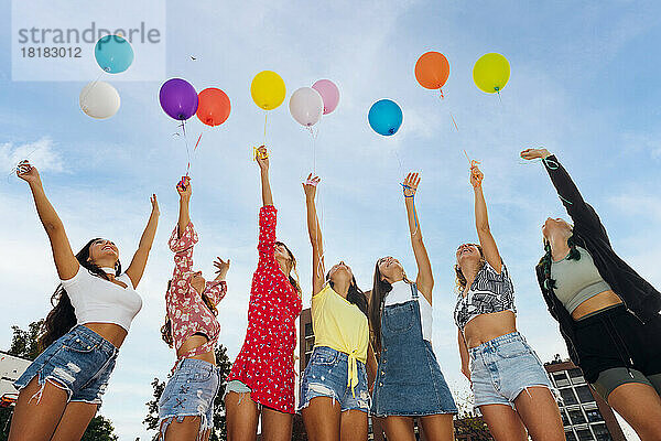 Freunde mit erhobenen Händen halten bunte Luftballons unter blauem Himmel