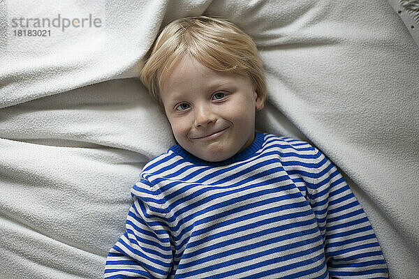 Porträt eines lächelnden kleinen Jungen  der zu Hause auf einer Decke liegt