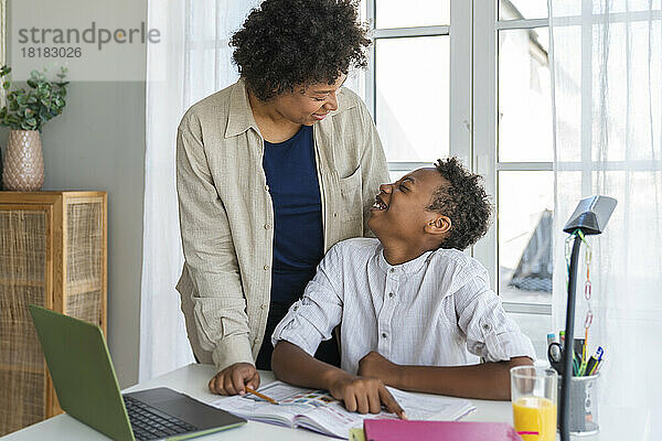 Glückliche Mutter spricht mit ihrem Sohn  der zu Hause am Arbeitstisch sitzt
