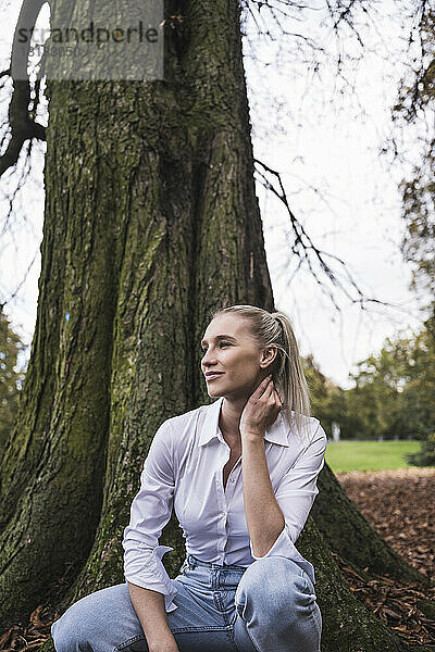 Junge Frau kauert vor Baum im Park