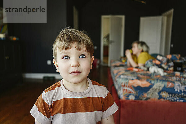 Cute boy in bedroom with brother in background at home