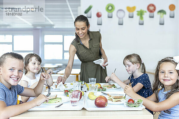 Lächelnde Schüler essen zusammen mit dem Lehrer in der Cafeteria zu Mittag