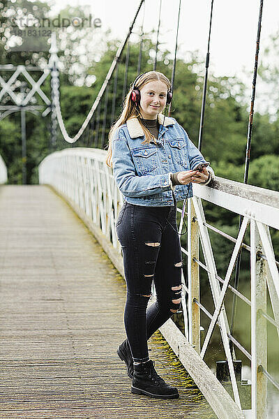 Teenagermädchen benutzt Smartphone und hört Musik auf einer Brücke