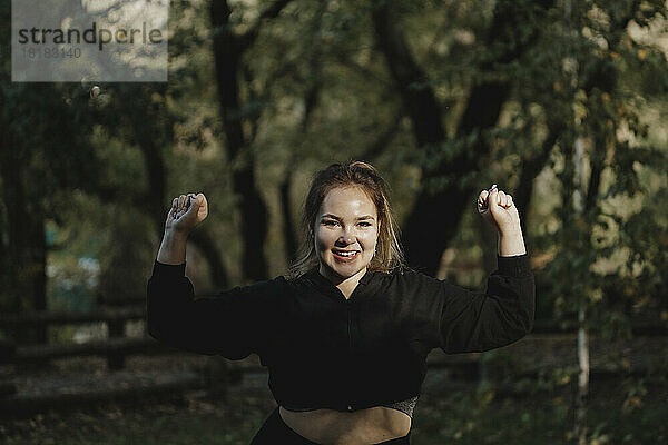 Glückliche junge Frau  die im dunklen Park ihre Muskeln spielen lässt