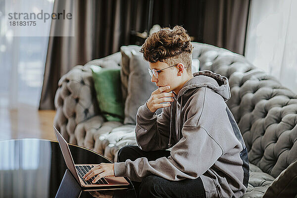 Student lernt mit Laptop auf dem Sofa im heimischen Wohnzimmer