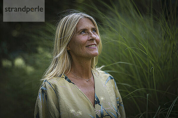 Lächelnde  nachdenkliche reife Frau mit blonden Haaren im Garten