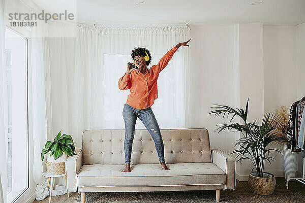 Sorgloser Freiberufler tanzt und singt auf dem Sofa im Heimbüro