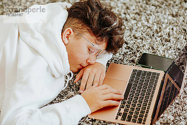Junge schläft vor Laptop auf Teppich