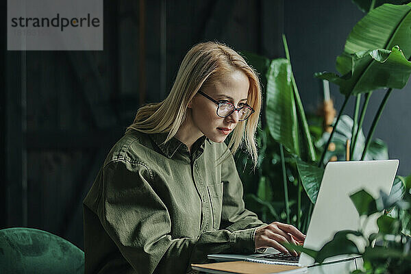 Entschlossene Geschäftsfrau mit Brille arbeitet im Heimbüro am Laptop