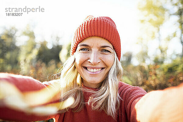 Lächelnde blonde reife Frau macht ein Selfie mit orangefarbener Strickmütze