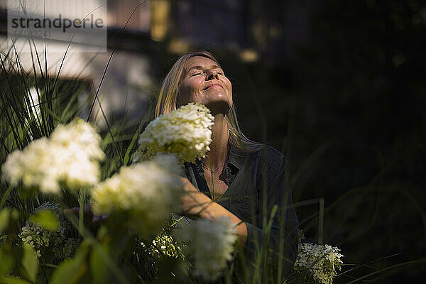 Reife Frau mit geschlossenen Augen genießt die Sonne im Garten