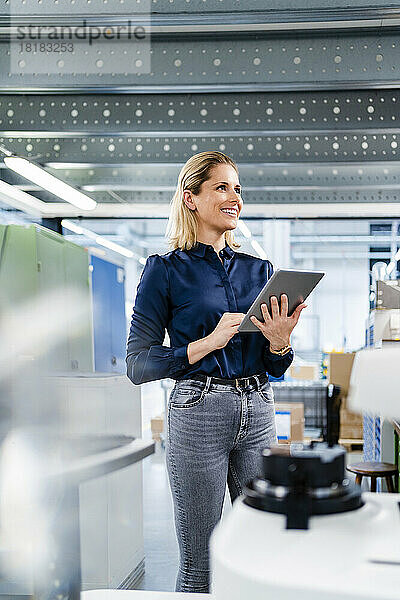 Lächelnde Geschäftsfrau mit Tablet-PC steht in der Fabrik