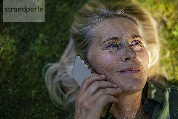 Lächelnde reife Frau  die im Garten mit dem Smartphone spricht