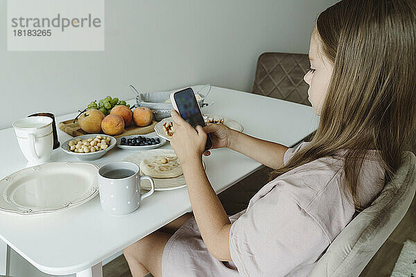 Mädchen fotografiert Frühstück auf Tisch mit Smartphone
