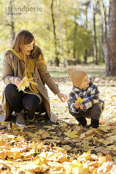 Glückliche Mutter und Sohn in hockender Position mit gelbem Blatt im Park