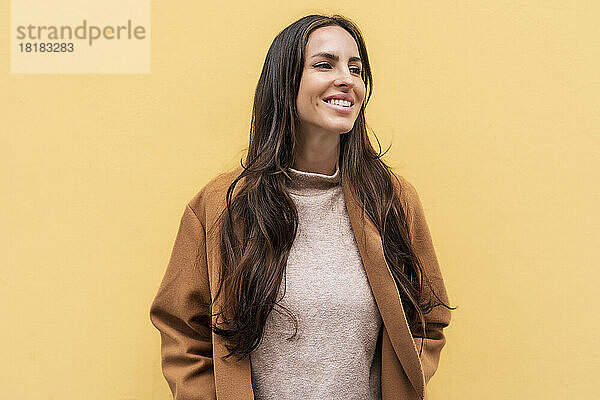 Lächelnde junge Frau vor gelber Wand
