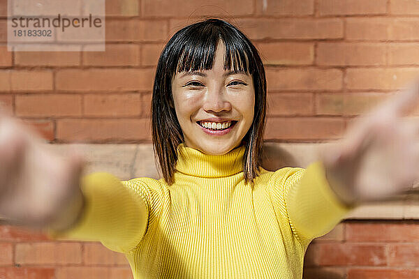 Glückliche junge Frau mit gelbem Rollkragenpullover vor einer Ziegelwand