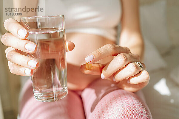 Werdende Frau hält Pille und trinkt Wasser an einem sonnigen Tag