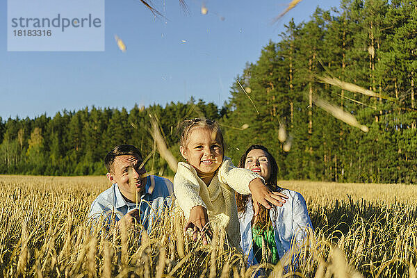 Glücklicher Vater und Mutter mit Tochter  die an einem sonnigen Tag Körner auf das Feld werfen