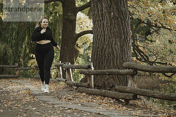 Lächelnde  übergroße Frau joggt im Herbstpark