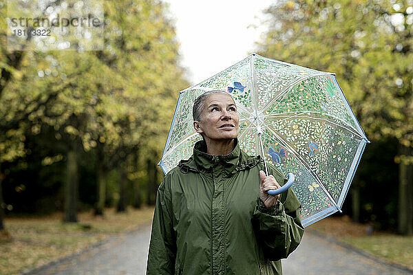 Nachdenkliche ältere Frau mit Regenmantel und Regenschirm